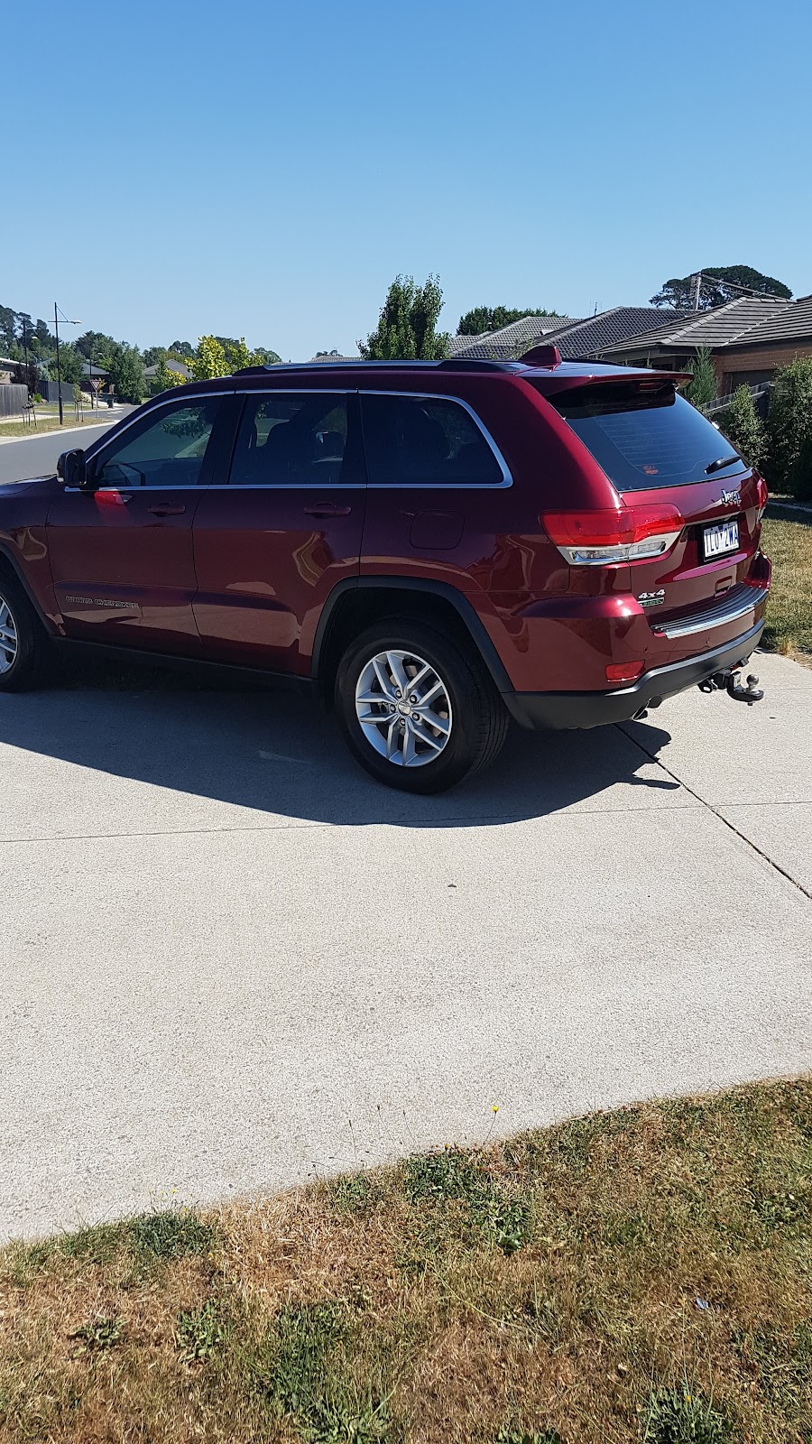 A maroon Jeep Grand Cherokee detailed on a customer's driveway